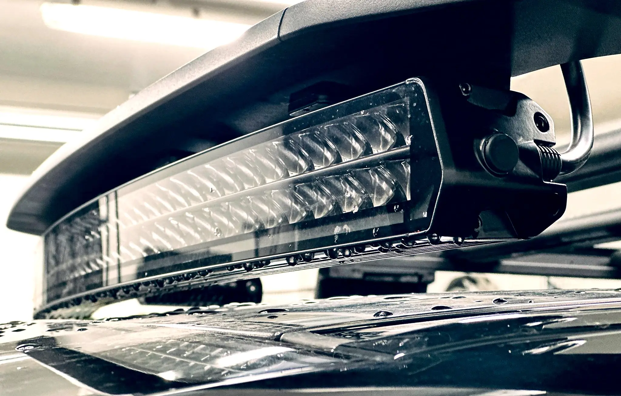 Curved Purelux LED lightbar mounted under the front edge of the roof rack, with water drops on the lens